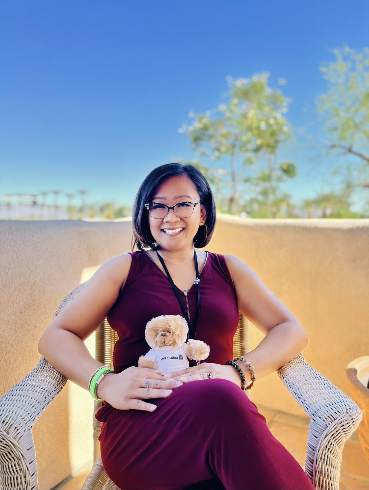 Woman smiling while sitting outdoors holding a stuffed toy.