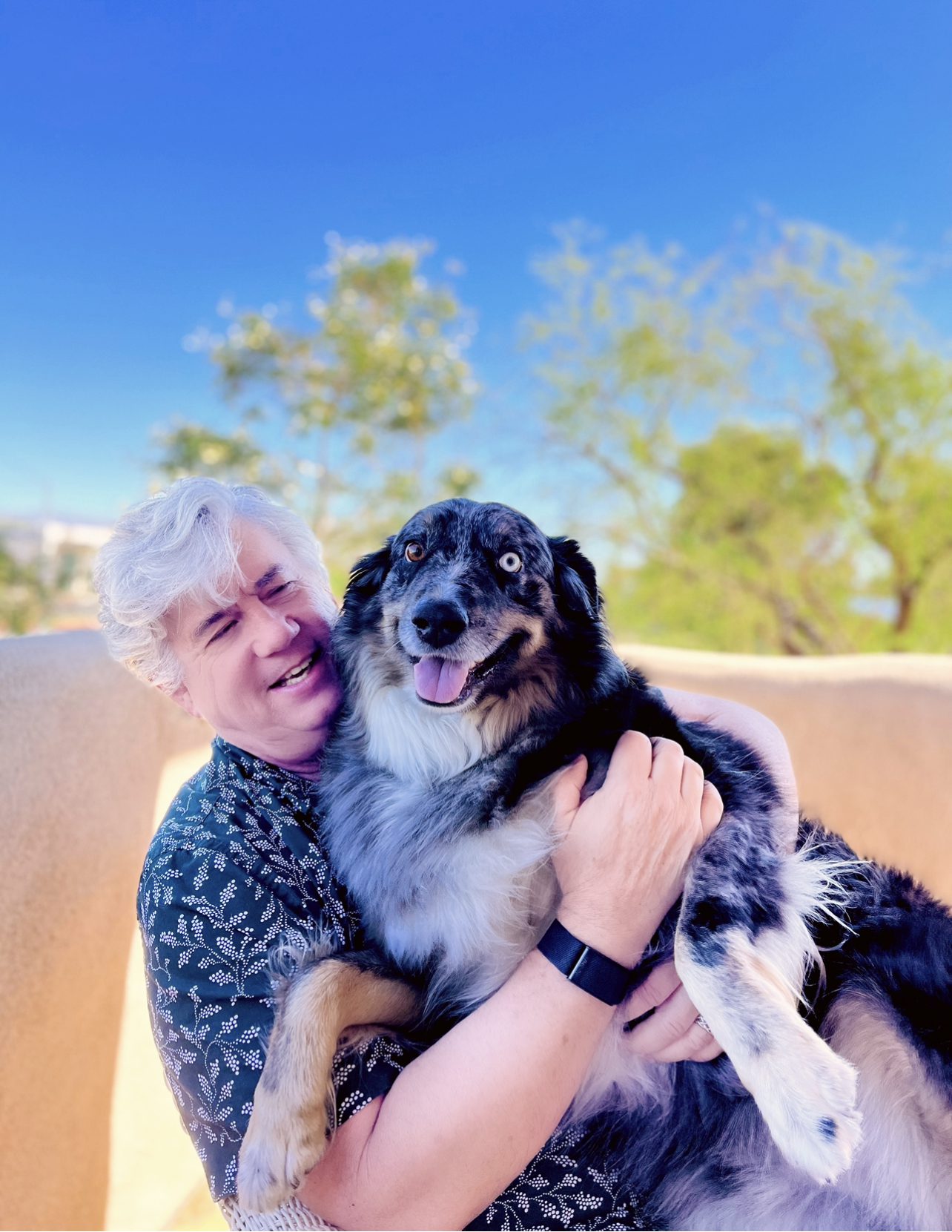 A person happily embracing a blue-eyed australian shepherd dog outdoors.