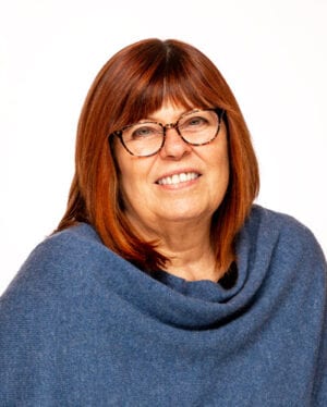 A smiling woman with brown hair, glasses, and a blue shawl against a white background.